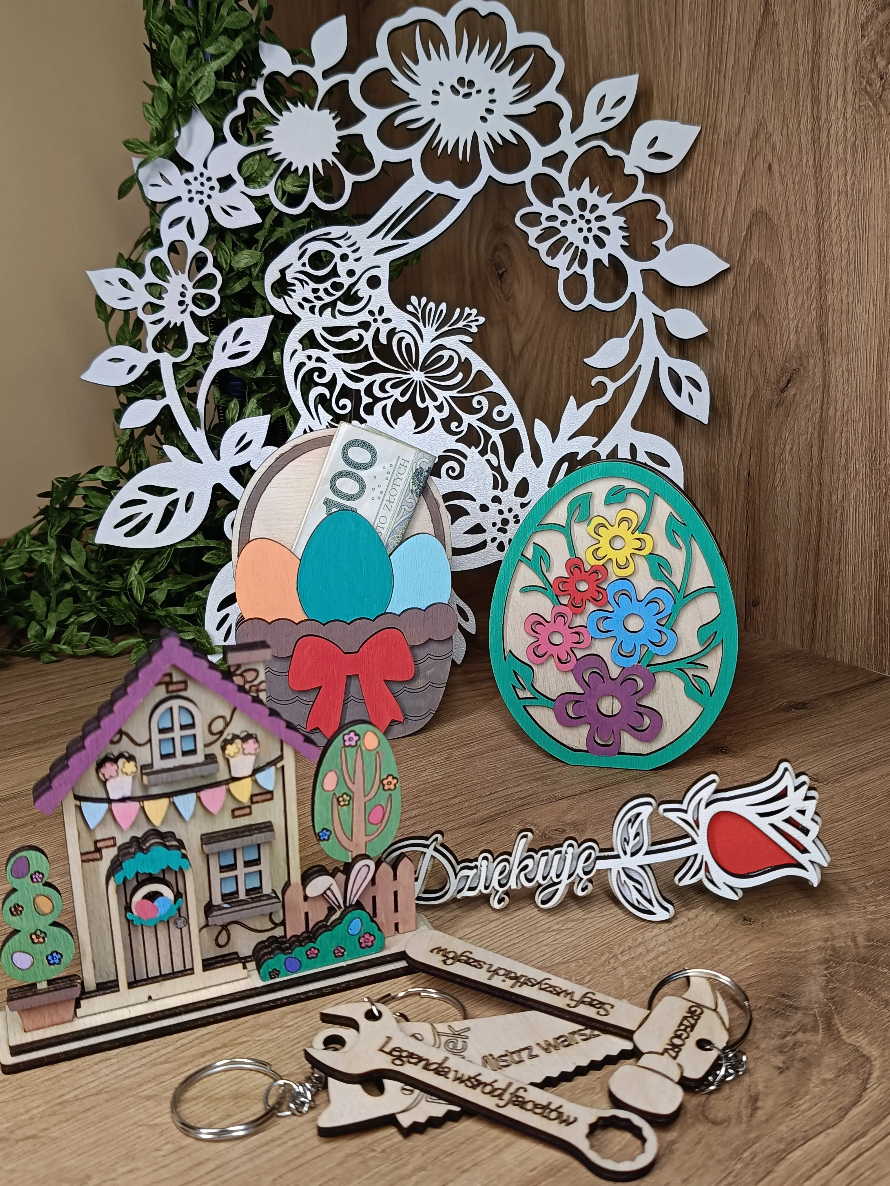 Wielkanocna kompozycja dekoracyjna z ażurowym królikiem, kolorowym jajkiem, koszyczkiem z pisankami i banknotem, domkiem oraz różą Dziękuję