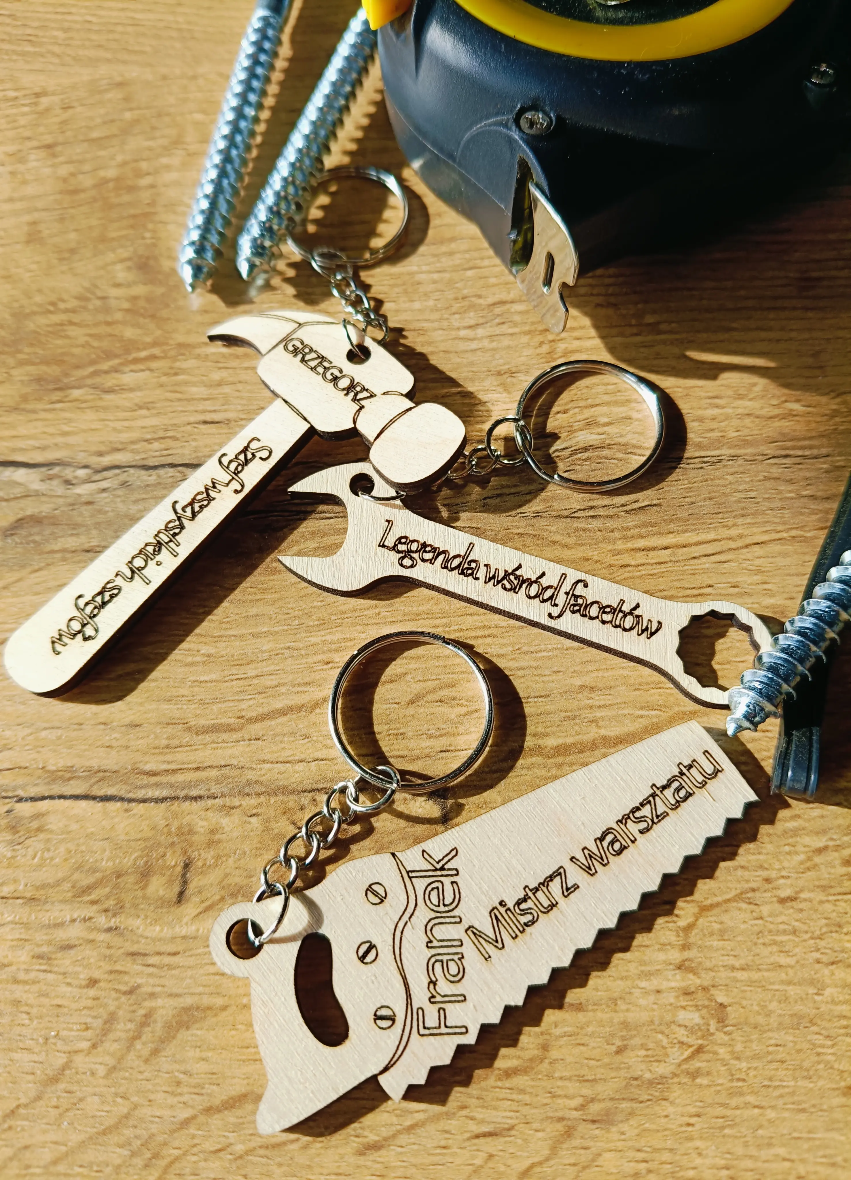 Drewniane breloki w kształcie młotka, klucza i piły z grawerami Gregory Szef wszystkich szefów, Legenda wśród fachowców oraz Mistrz warsztatu Franek