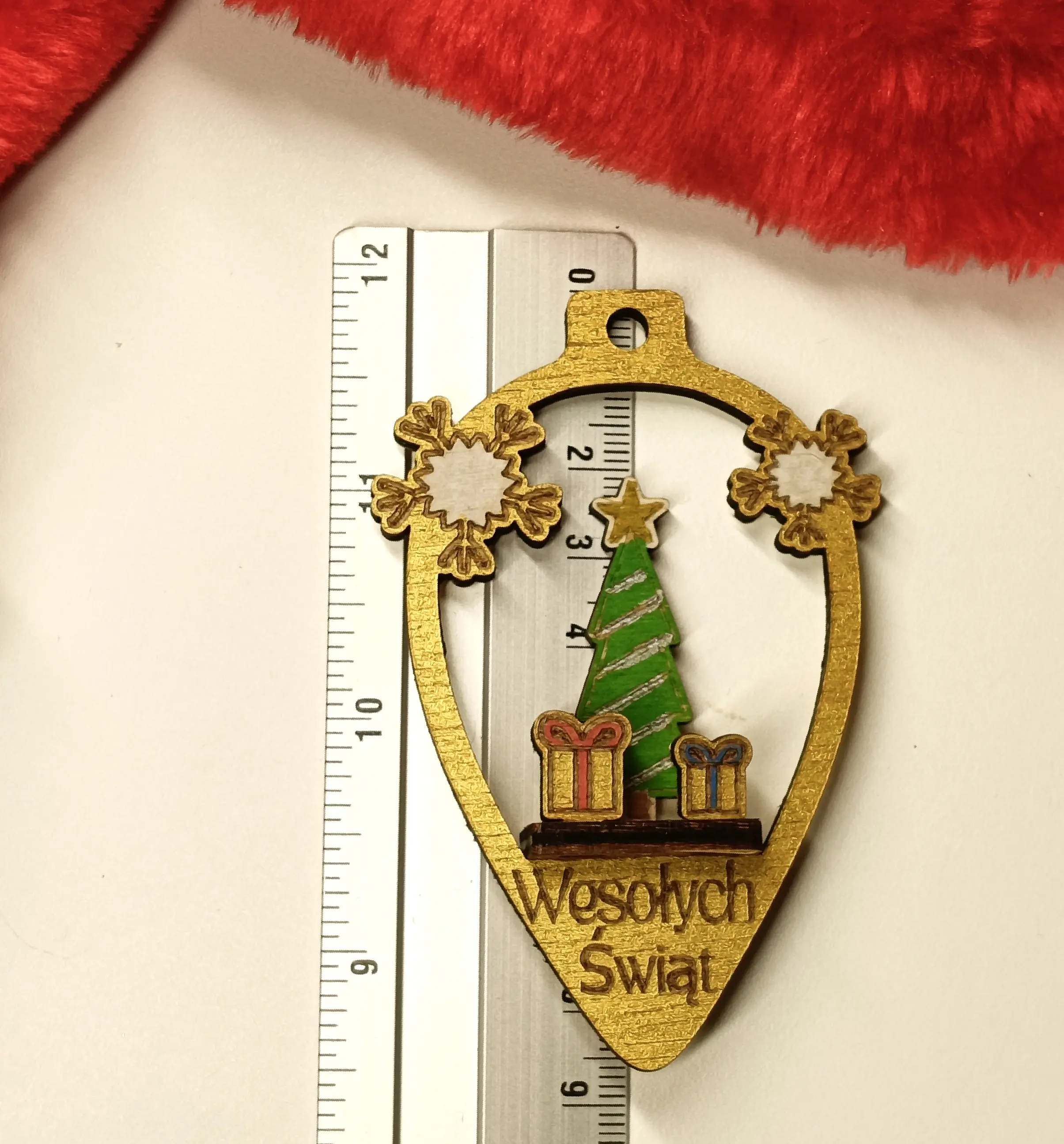 Drewniana bombka świąteczna w kształcie łezki z grawerem Wesołych Świąt, ozdobiona choinką, prezentami i śnieżynkami