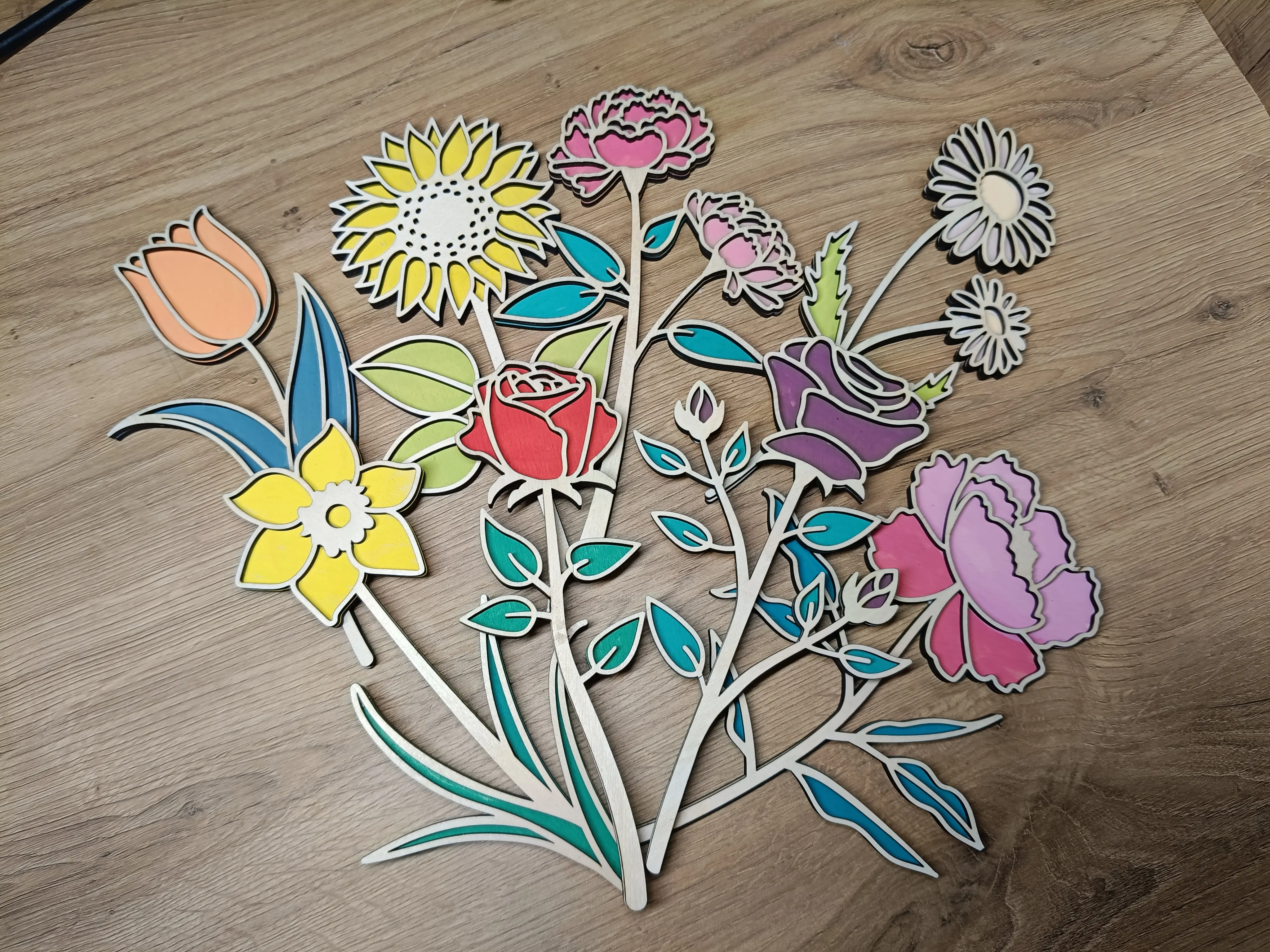 Kolorowe wycinanki kwiatowe przedstawiające słoneczniki, róże, tulipany i stokrotki ułożone na drewnianym tl