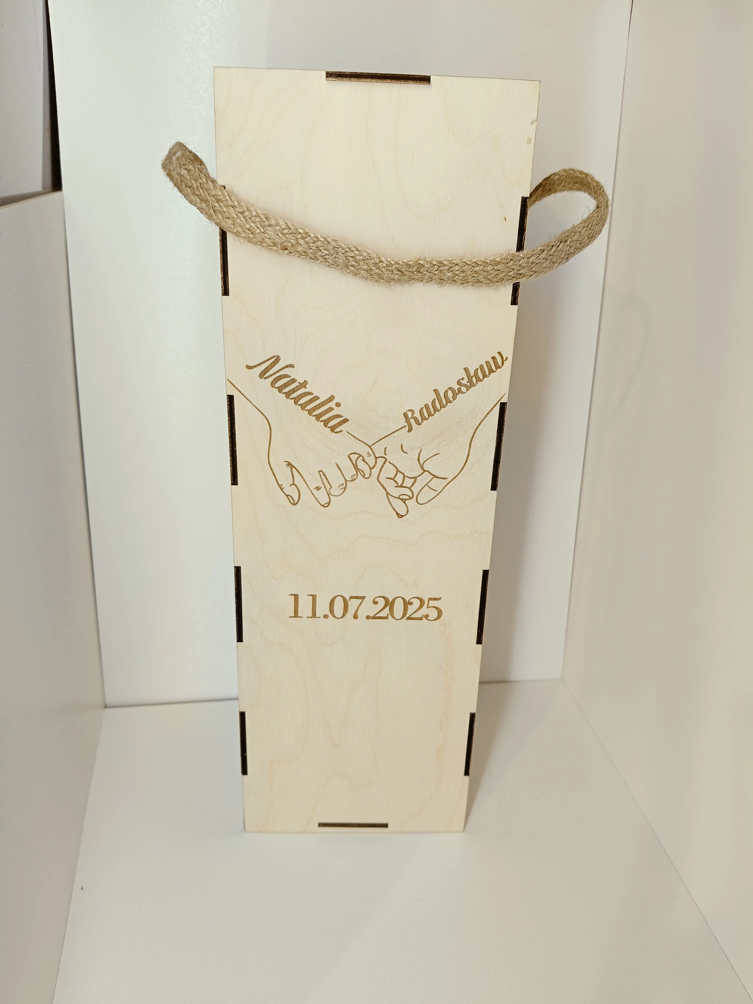 Drewniane pudełko na butelkę z rączką ze sznurka, grawerem Natalia & Radosław, datą 11.07.2025 i motywem splecionych dłoni
