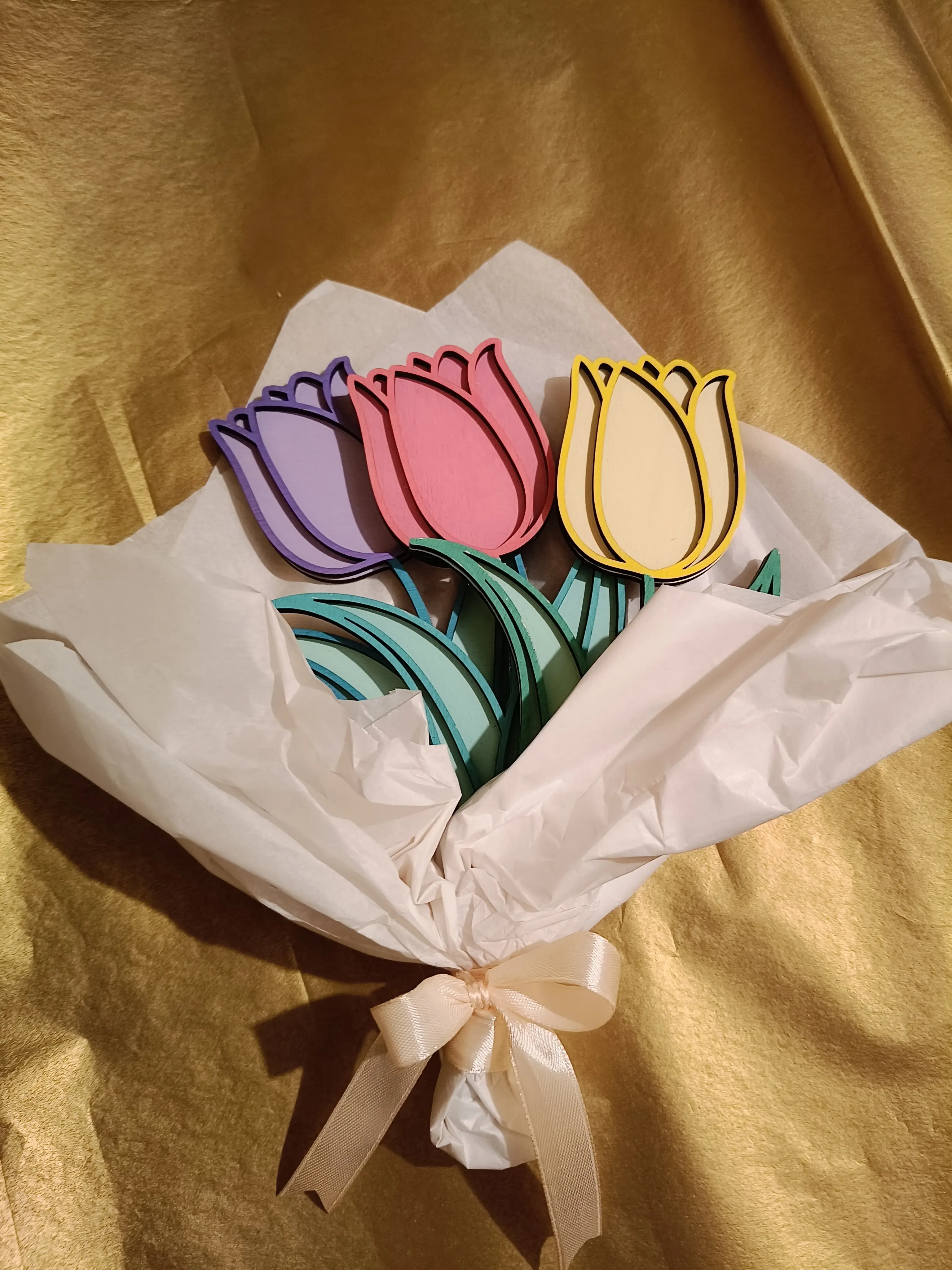Papierowy bukiet tulipanów w kolorach fioletowym, różowym, żółtym i czerwonym, owinięty białą bibułą i przewiązany kremową wstążką